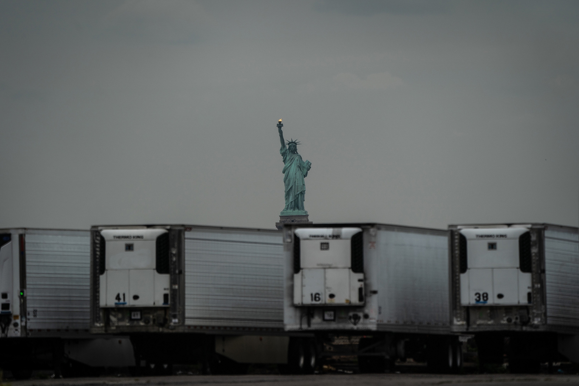 Statue of Liberty behind coronavirus temporary refrigerated morgue trailers
