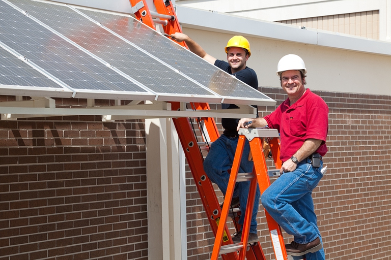Happy electricians employed to install energy efficient solar panels in the new green economy.