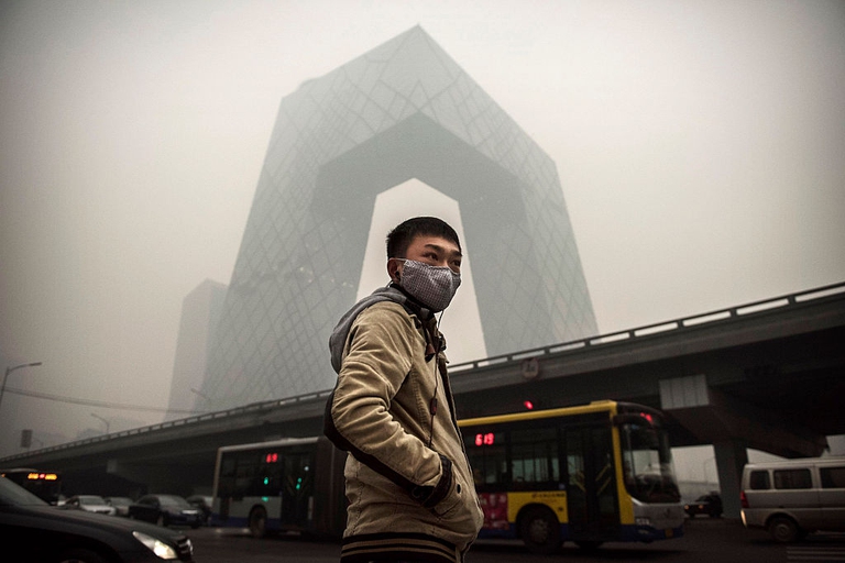 A Chinese man wears a mask as he waits to cross the road near the CCTV building during heavy smog  in Beijing, China. In 2014, United States President Barack Obama and China's president Xi Jinping agreed on a plan to limit carbon emissions by their countries, which are the world's two biggest polluters, at a summit in Beijing. © Kevin Frayer/Getty Images)
