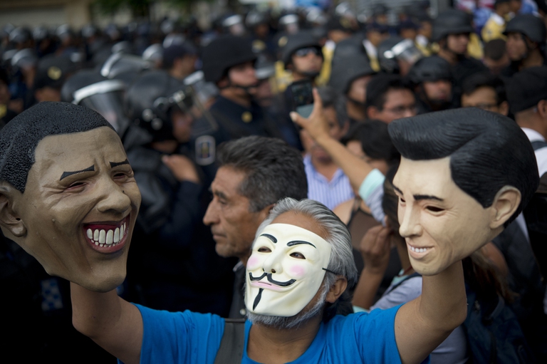 A masked teacher on strike raises masks of US President Barrack Obama (L) and Mexico's President Enrique Pena Nieto (R) in front of riot policemen during a demonstration in Mexico City on July 5, 2016. /AFP /YURI CORTEZ/Getty Images