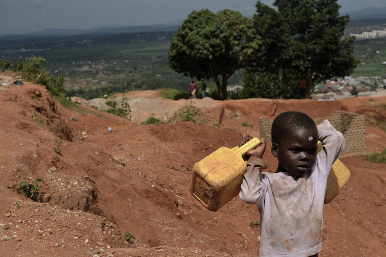 Un bambino si dirige alla fonte a riempire le taniche d'acqua