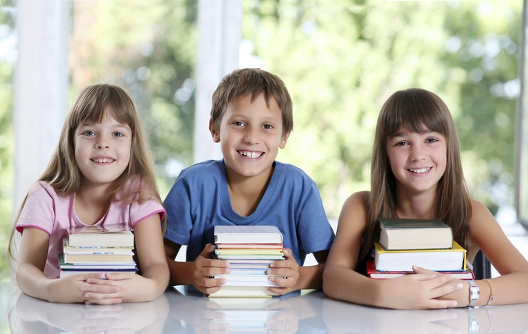 Happy schoolchildren with many books sitting in classroom.
