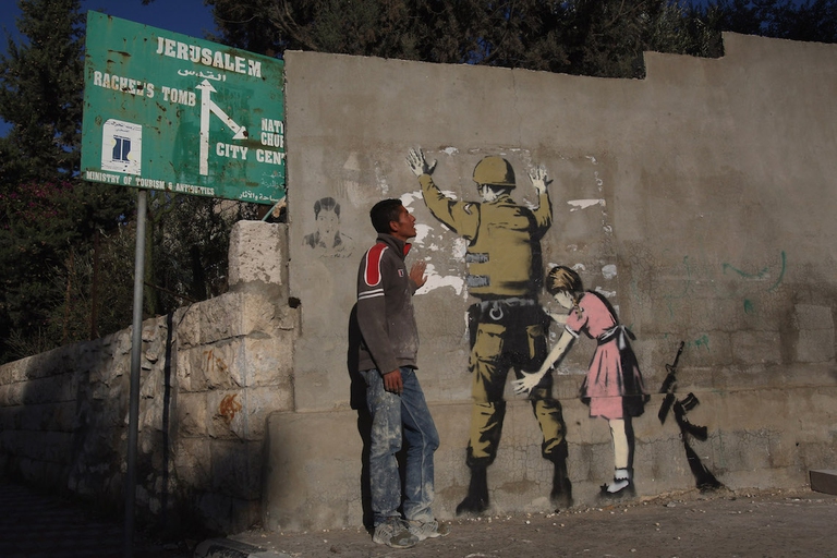 Un ragazzo guarda un graffito di Banksy a Betlemme.