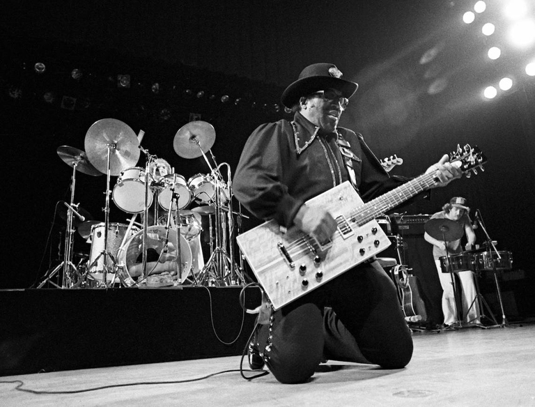 Bo Diddley inginocchiato sul palco suona la sua "Cigar Box".